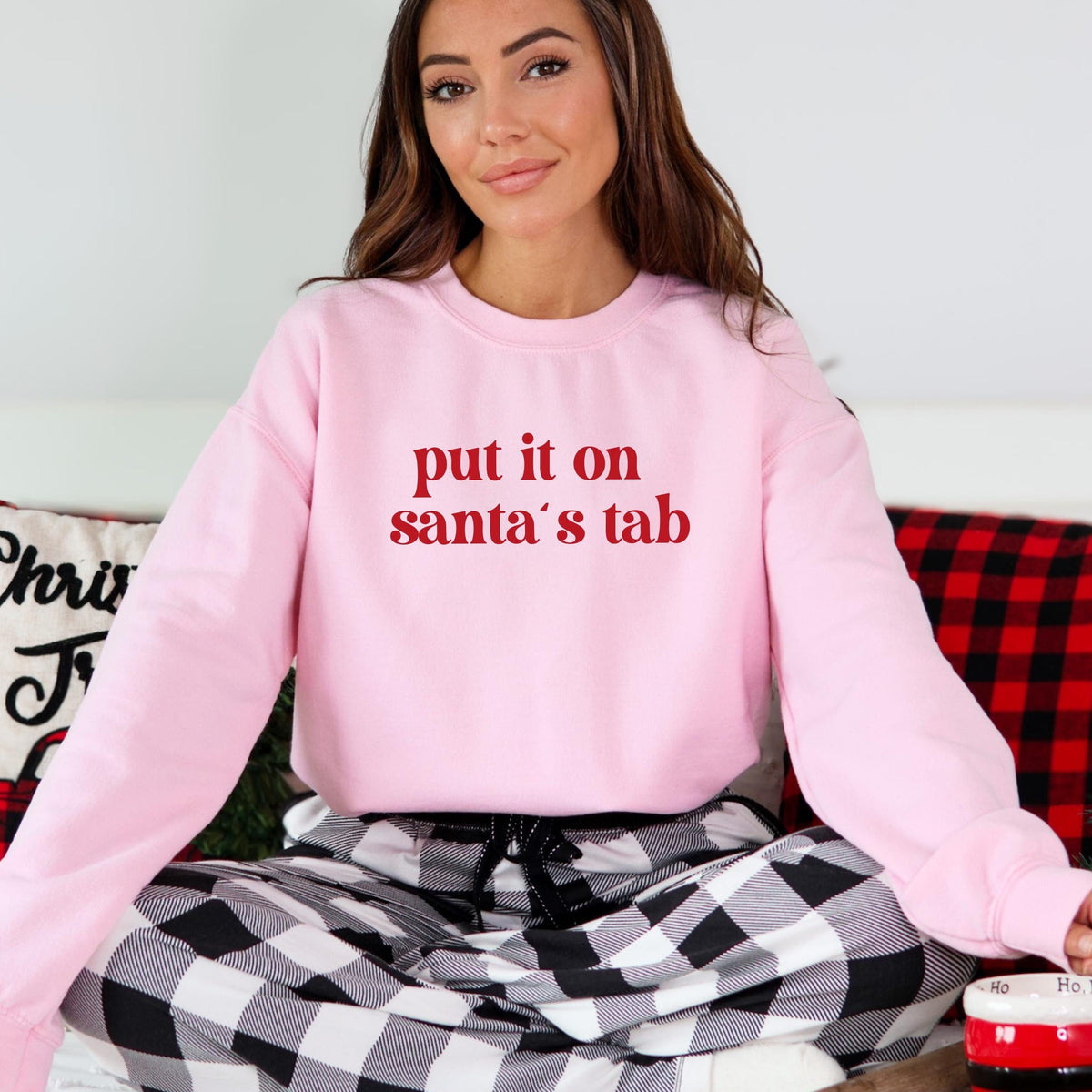 Model wearing a pink crewneck sweatshirt with put it on santa's tab in red lettering